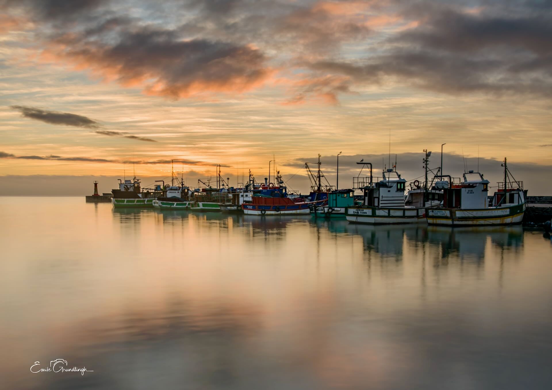 Kalk Bay colourful fishing fleet moored in glassy harbour water at golden sunrise with soft pink clouds