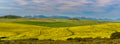 Panoramic rolling canola and wheat hills with layered mountain ranges in the hazy distance
