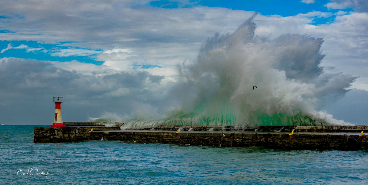The Green Monster – massive emerald wave crashing over Kalk Bay harbour wall and lighthouse