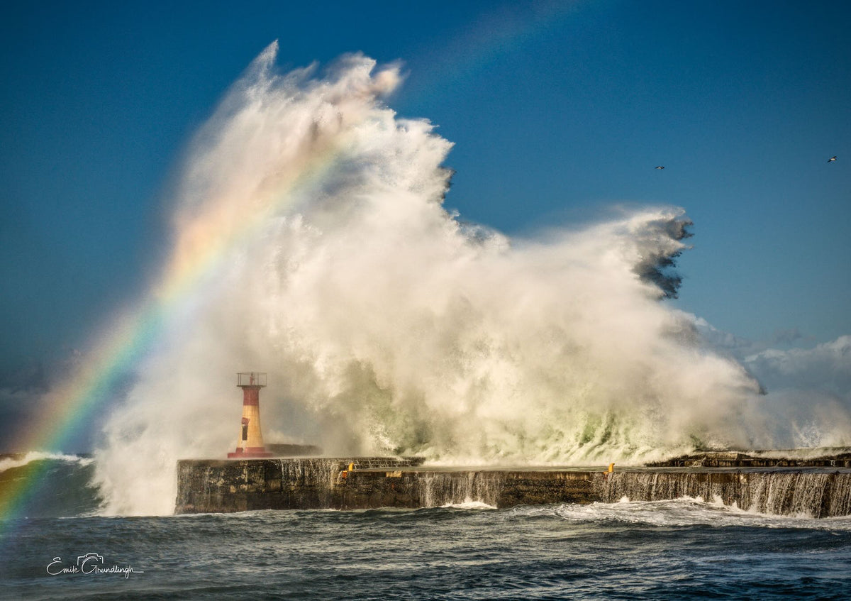 Rainbow Over the Storm – giant wave engulfing Kalk Bay lighthouse with rainbow in spray