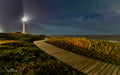 Slangkop After Dark – Slangkop Lighthouse beam at night with starry sky and boardwalk through fynbos