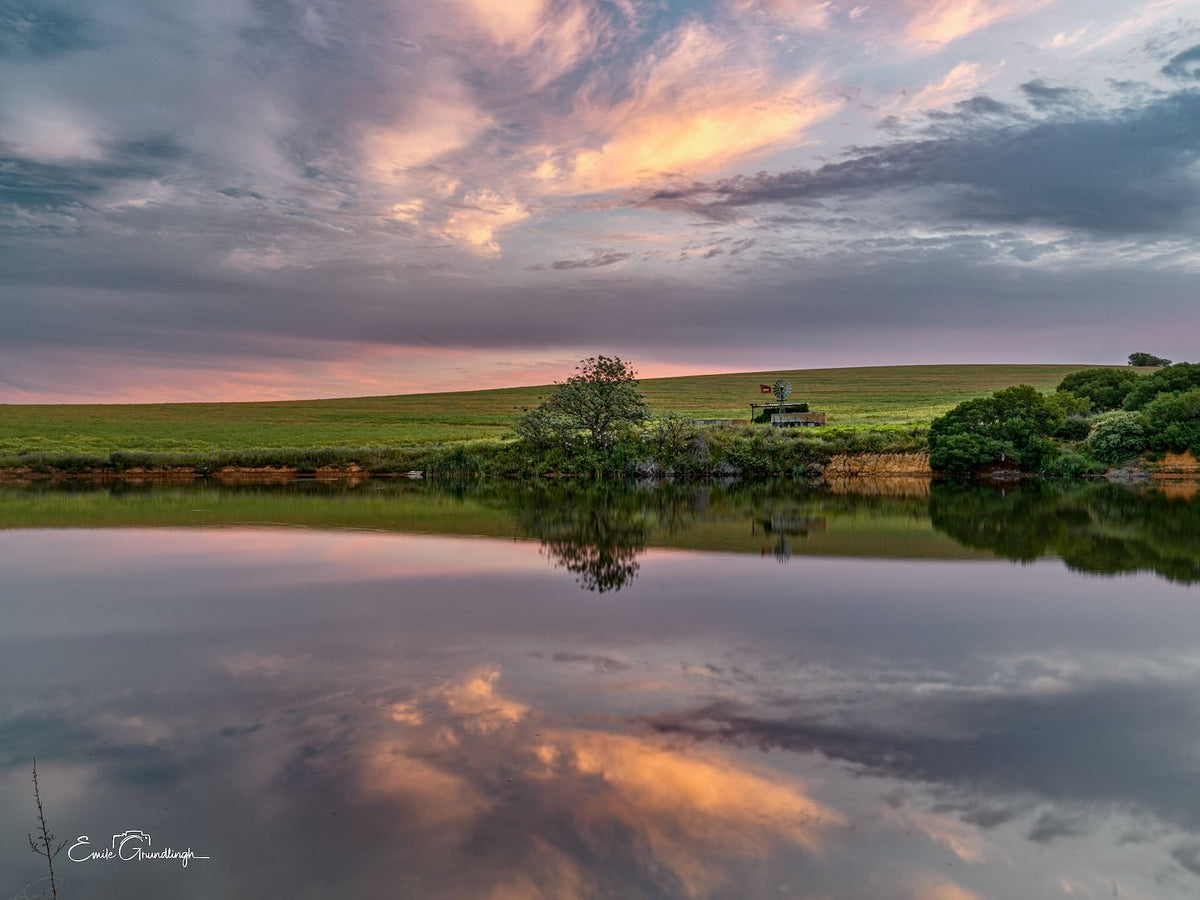 Peach-gold clouds, trees and a distant windmill reflected in still water outside Riebeek Kasteel, photographed by Emile Grundlingh.
