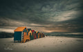 Colourful Muizenberg beach huts under a dark stormy sky