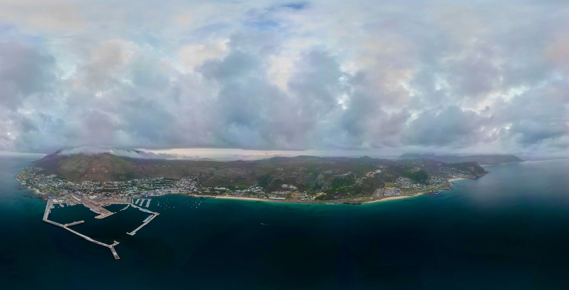 Aerial panorama of the Deep South peninsula showing Simon's Town marina, Boulders Beach and mountain range under dramatic clouds over False Bay