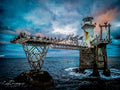 Roman Rock Lighthouse with steel gantry bridge covered in Cape cormorants under dramatic teal storm sky, False Bay