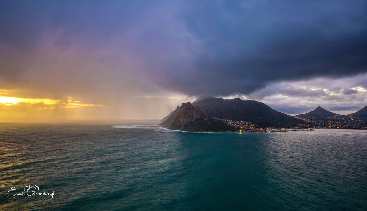 Storm rolling over Hout Bay headland at sunset with rain curtains and harbour lights by Emile Grundlingh