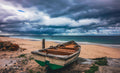 Weathered green and white rowing boat abandoned on golden sand facing stormy False Bay with dramatic dark clouds overhead