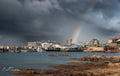 Rainbow arcing over Kalky's fish and chips restaurant at Kalk Bay harbour with fishing boats and cormorants under dramatic storm sky