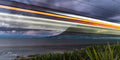 Long exposure light trails of coastal train blazing past with False Bay and Fish Hoek mountain silhouette beneath dramatic storm clouds