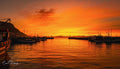 Kalk Bay harbour glowing in intense all-over orange and crimson sunset with fishing fleet silhouetted and lighthouse in distance