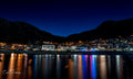 Kalk Bay village at night with colourful lights reflecting in still harbour water and stars in deep navy sky above mountain silhouette