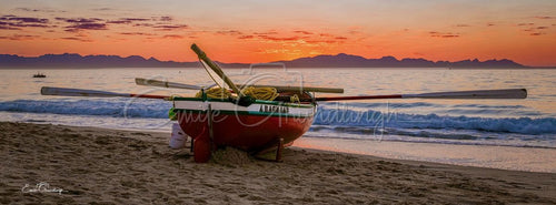 The red rowing boat A Ragnaar on the sand as the sun sets in orange and crimson over False Bay and the mountains