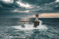 Roman Rock Lighthouse battered by waves with collapsed gantry arm and dramatic god-rays through storm clouds, False Bay