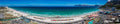 High aerial panorama of Muizenberg Beach showing colourful beach huts, waterpark, crowds and full sweep of False Bay with mountain ranges