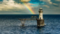 Perfect rainbow arcing down onto Roman Rock Lighthouse with cormorants on gantry against dramatic storm clouds over False Bay