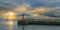 Kalk Bay harbour wall lighthouse with golden sun rays through storm clouds over False Bay