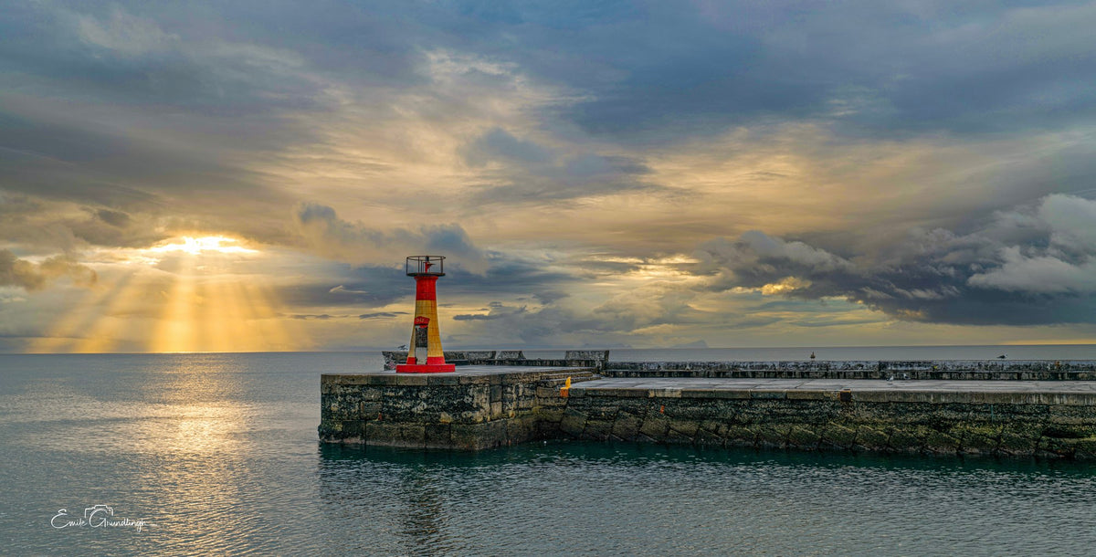 Kalk Bay harbour wall lighthouse with golden sun rays through storm clouds over False Bay
